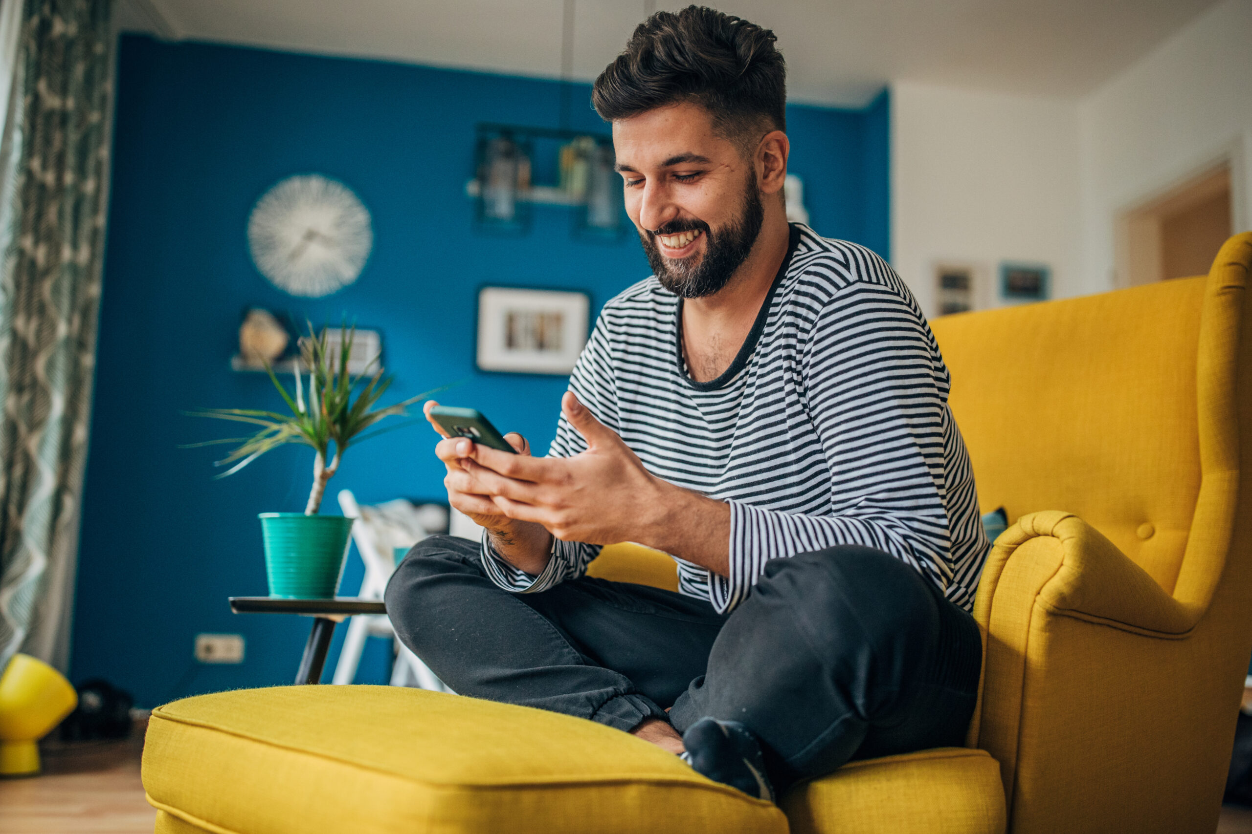Man sitting at home in his armchair and using mobile phone.