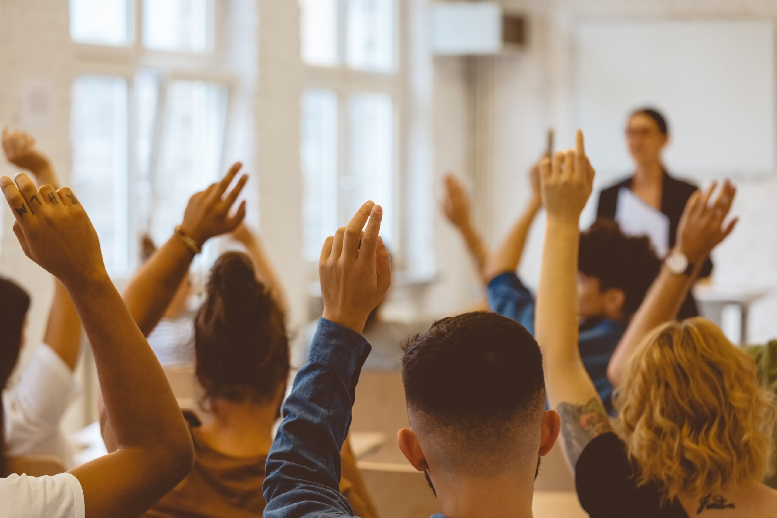 Rear view of students raising their hands in a classroom.