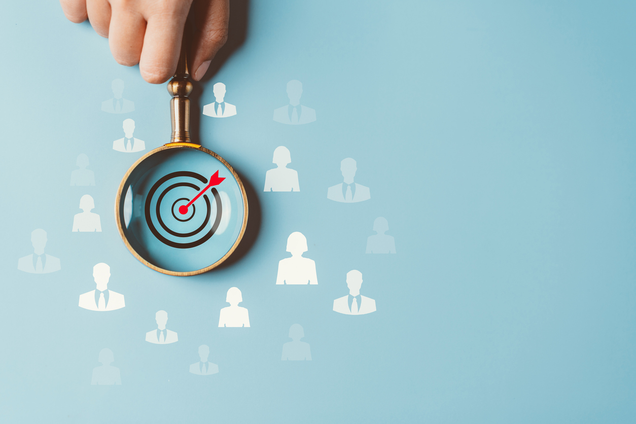 Magnifying glass over bulls-eye in a crowd of people.